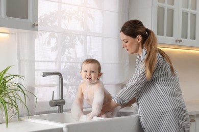 Mother washing her little baby in sink at home