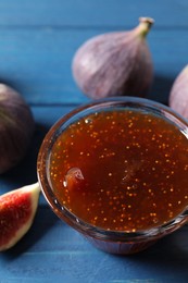 Glass bowl with tasty sweet jam and fresh figs on blue wooden table, closeup