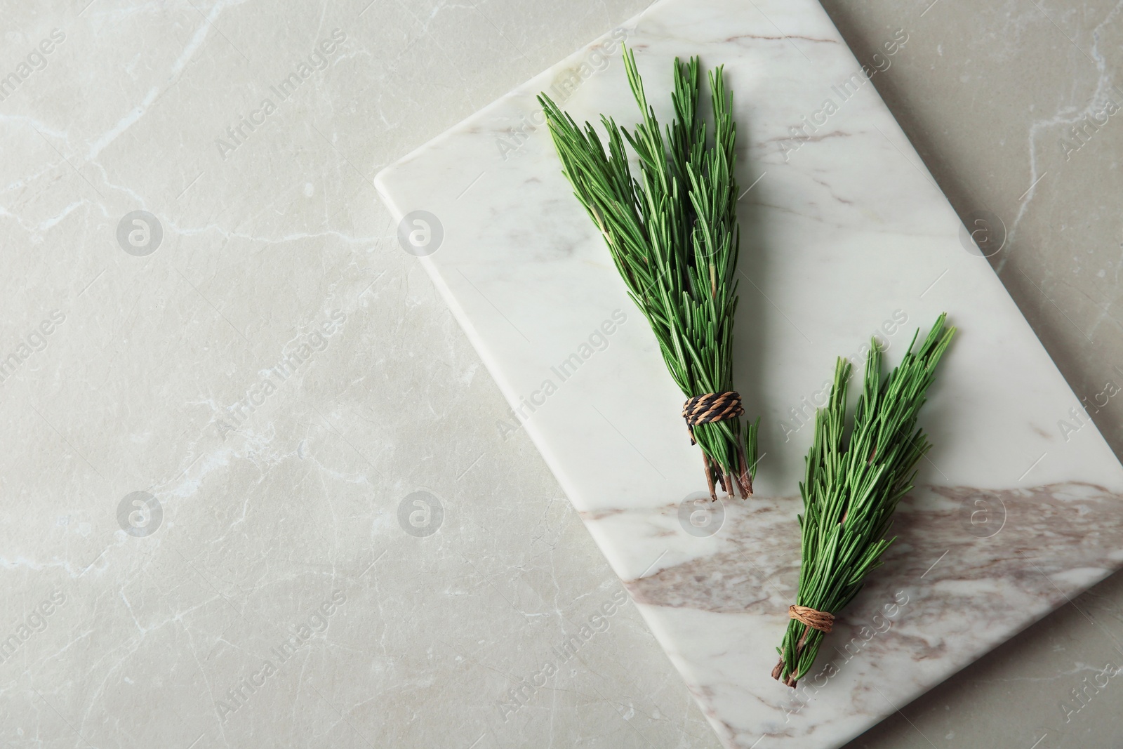 Photo of Board with bundles of fresh rosemary twigs on grey marble background, top view. Space for text