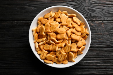 Delicious goldfish crackers in bowl on black wooden table, top view