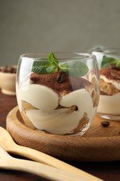 Photo of Delicious tiramisu in glasses, mint leaves, coffee beans and spoon on table, closeup