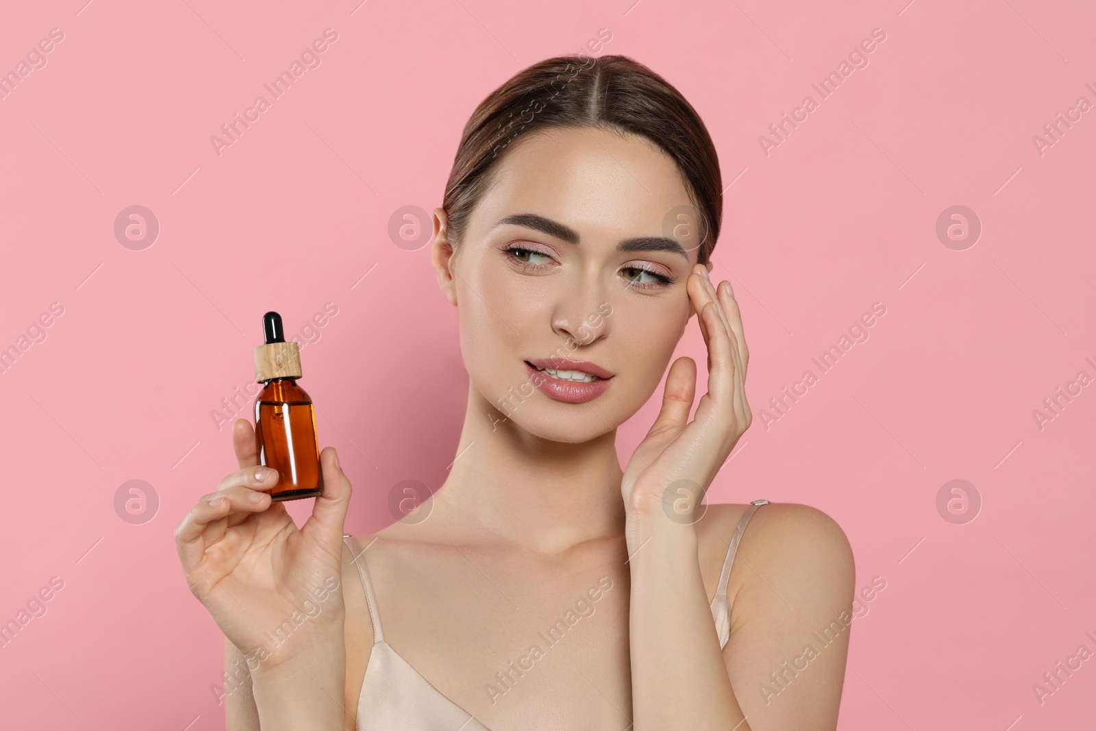 Photo of Young woman with bottle of essential oil on pink background