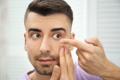 Photo of Young man putting contact lens in his eye indoors