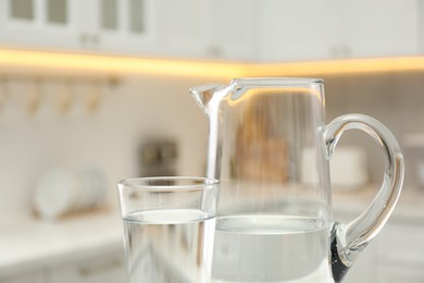 Photo of Jug and glass with clear water in kitchen, closeup