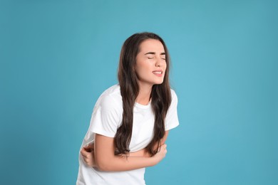 Photo of Young woman suffering from stomach ache on light blue background. Food poisoning
