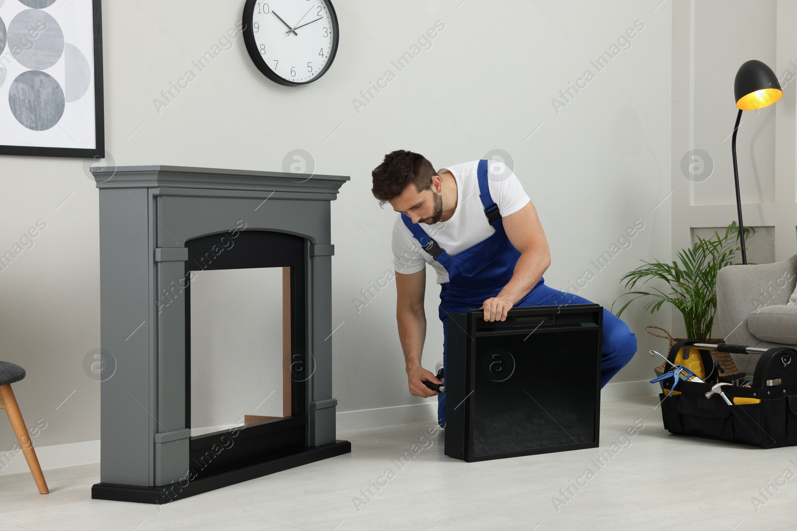 Photo of Professional technician with screwdriver installing electric fireplace in room