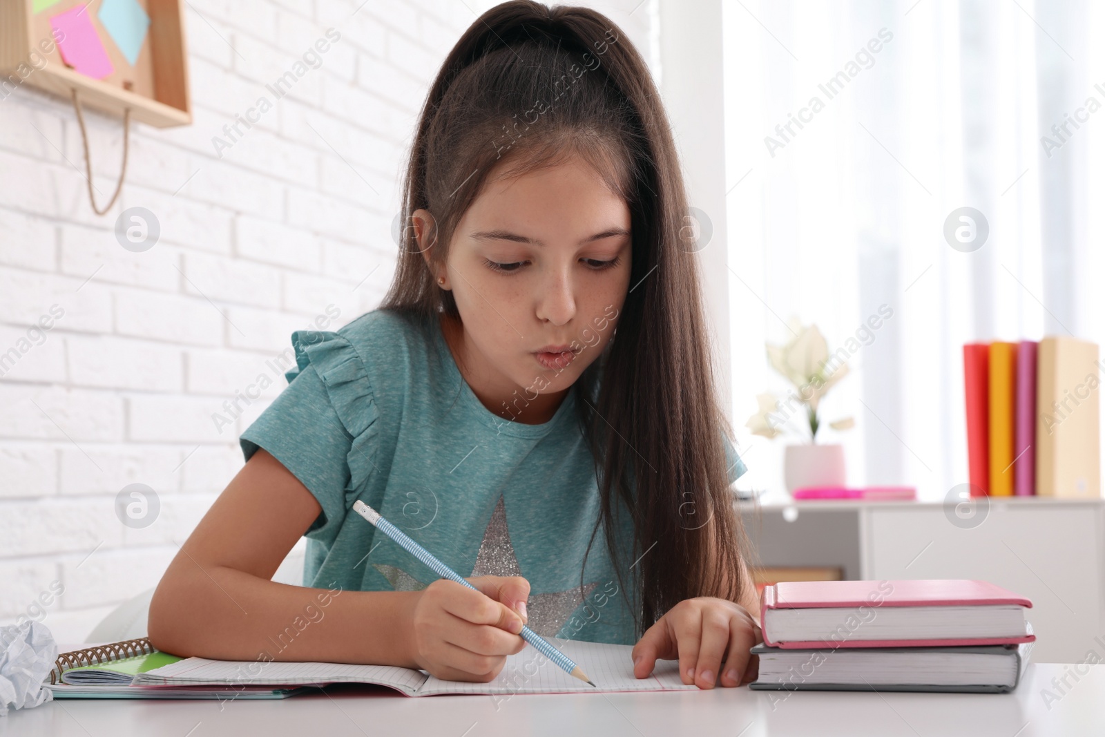 Photo of Pretty preteen girl doing homework at table