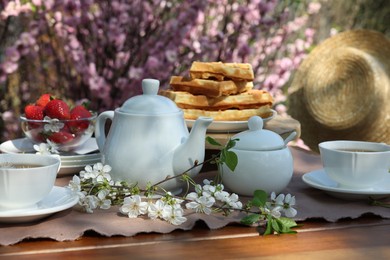 Photo of Beautiful spring flowers, freshly baked waffles and ripe strawberries on table served for tea drinking in garden