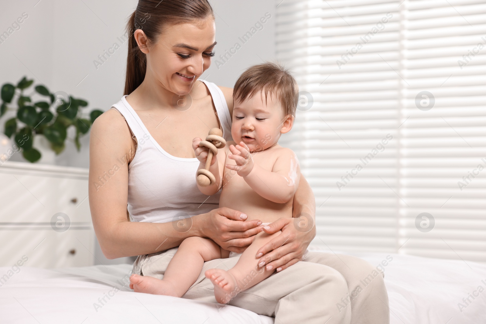 Photo of Happy mother holding her baby with body cream on skin at home