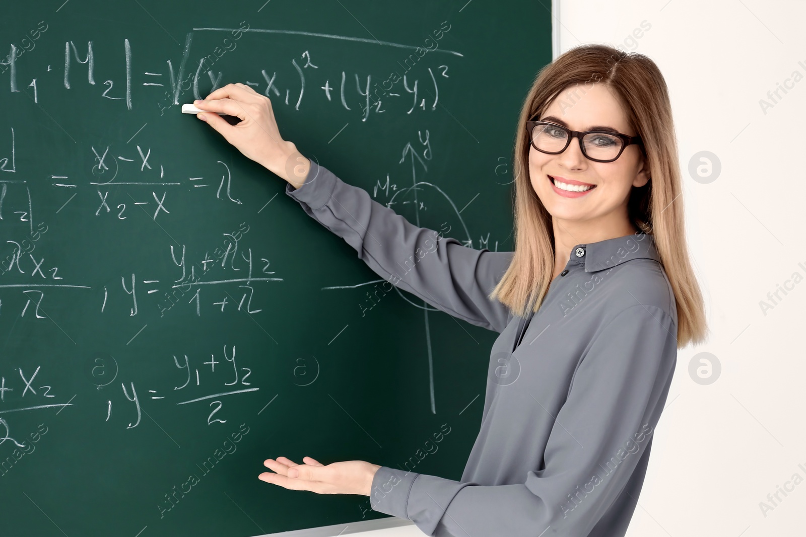 Photo of Young female teacher writing on blackboard in classroom