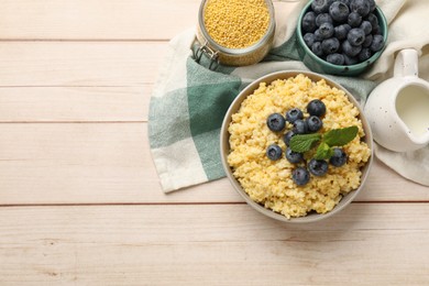 Photo of Tasty millet porridge with blueberries and mint in bowl on light wooden table, flat lay. Space for text