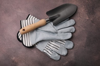 Gardening gloves and trowel on brown textured table, top view