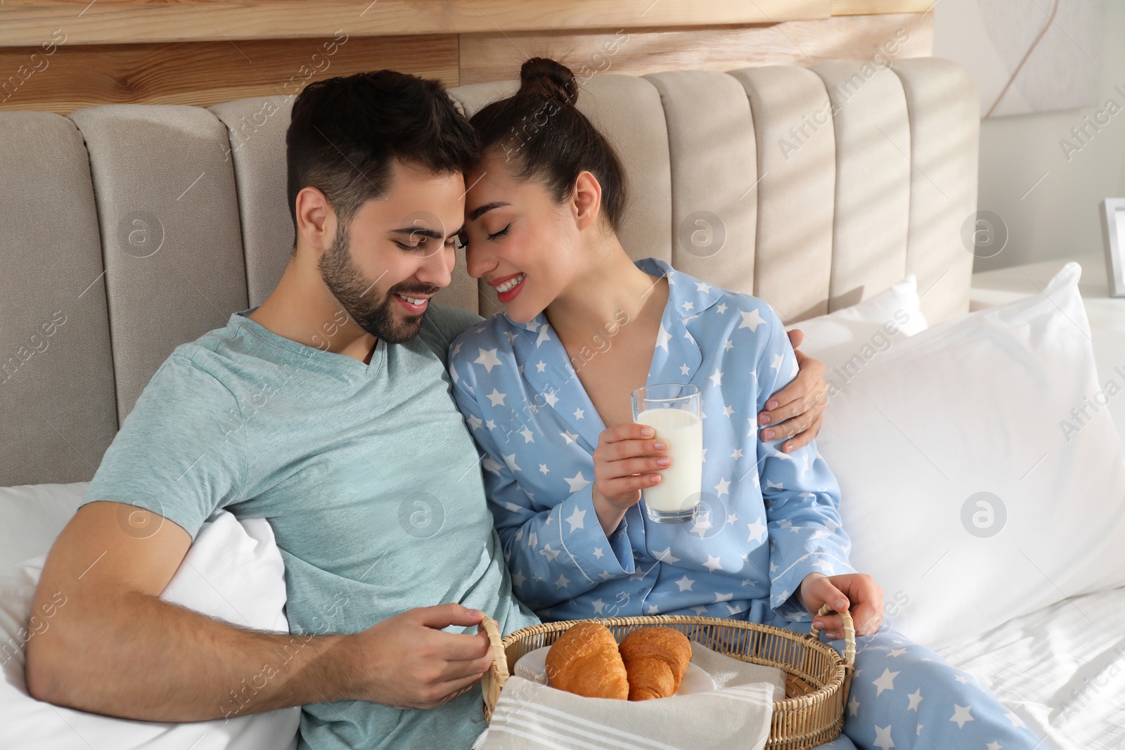 Photo of Happy couple in pajamas having breakfast on bed at home