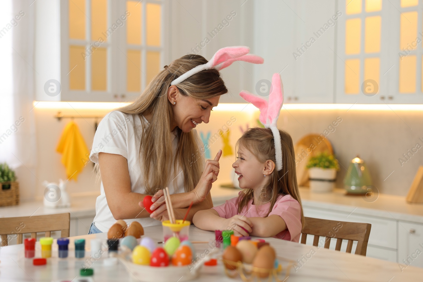 Photo of Easter celebration. Mother with her cute daughter having fun while painting eggs at white marble table in kitchen