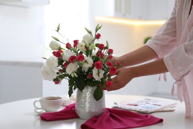 Woman with bouquet of fresh flowers in stylish vase at table, closeup