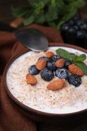 Tasty wheat porridge with milk, blueberries and almonds in bowl on table, closeup