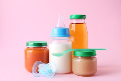 Healthy baby food, juice, milk, pacifier and spoon on pink background