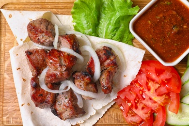 Tasty shish kebab and sauce on wooden board, top view