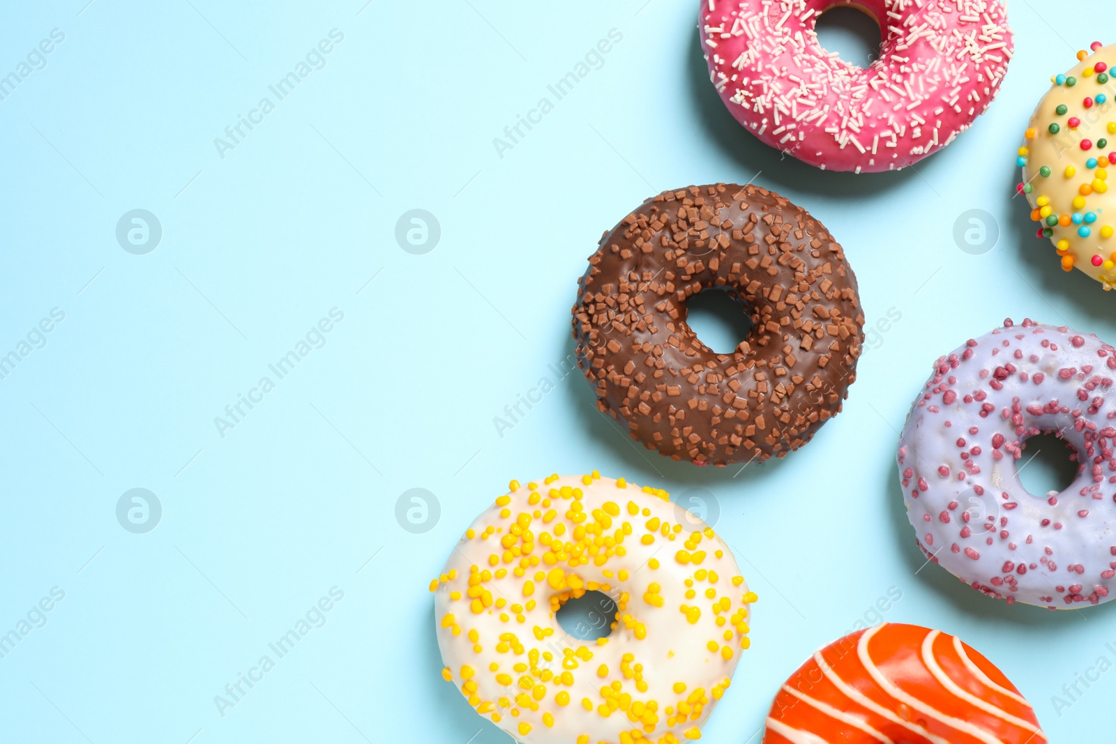 Photo of Delicious glazed donuts on light blue background, flat lay. Space for text