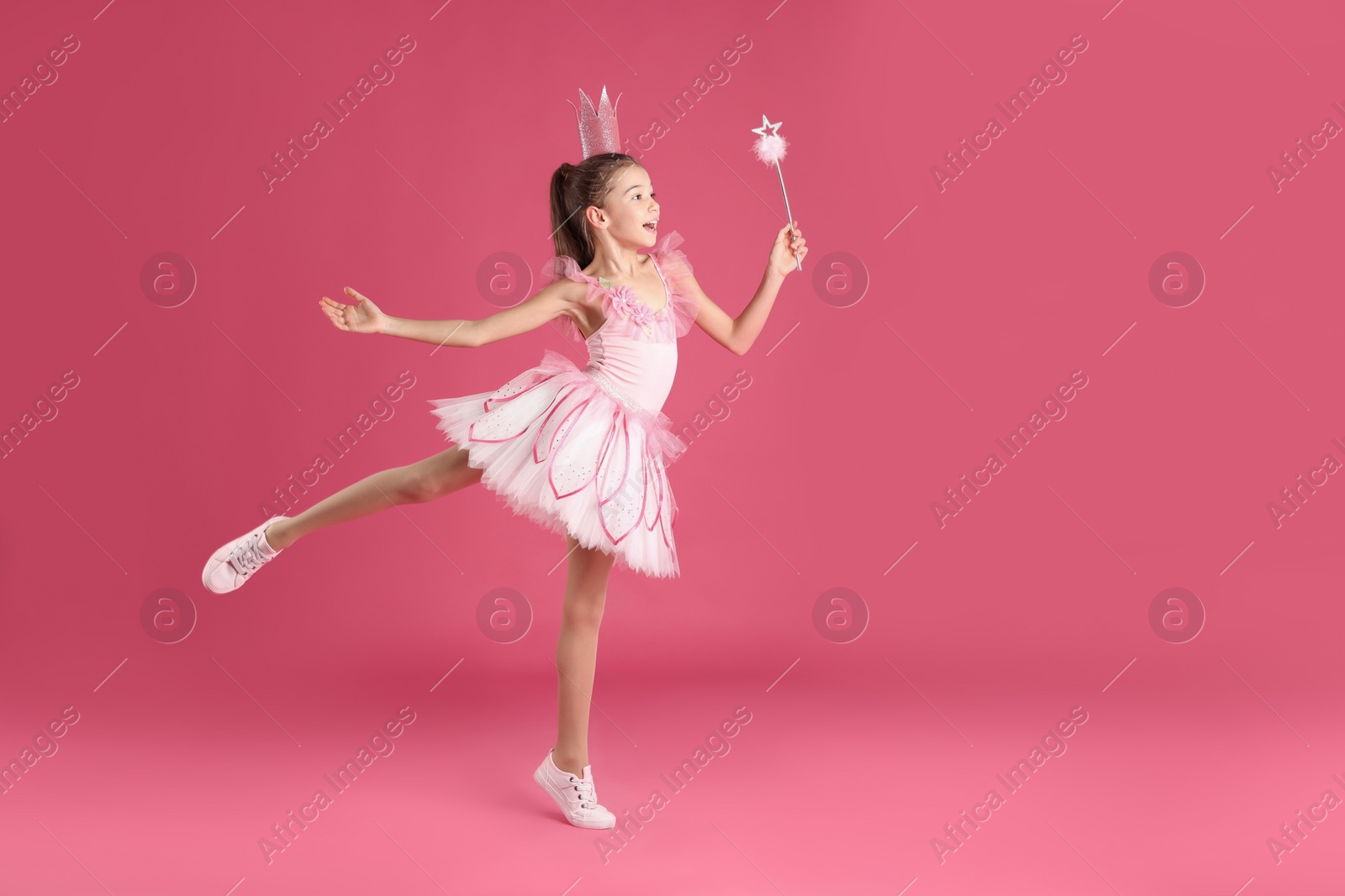 Photo of Cute girl in fairy dress with crown and magic wand on pink background, space for text. Little princess