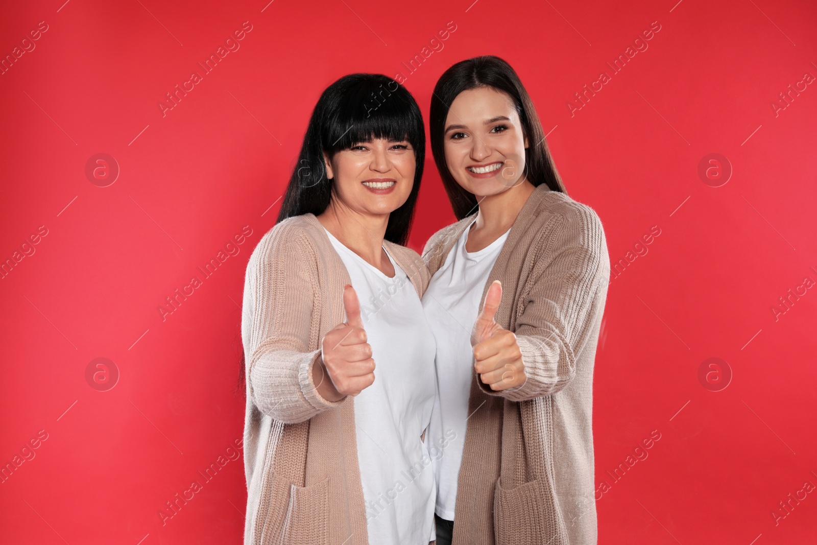 Photo of Young daughter and her mature mother showing thumbs up on color background