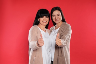 Young daughter and her mature mother showing thumbs up on color background