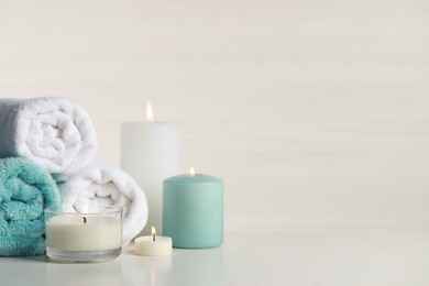 Photo of Beautiful spa composition with burning candles and rolled towels on white table. Space for text