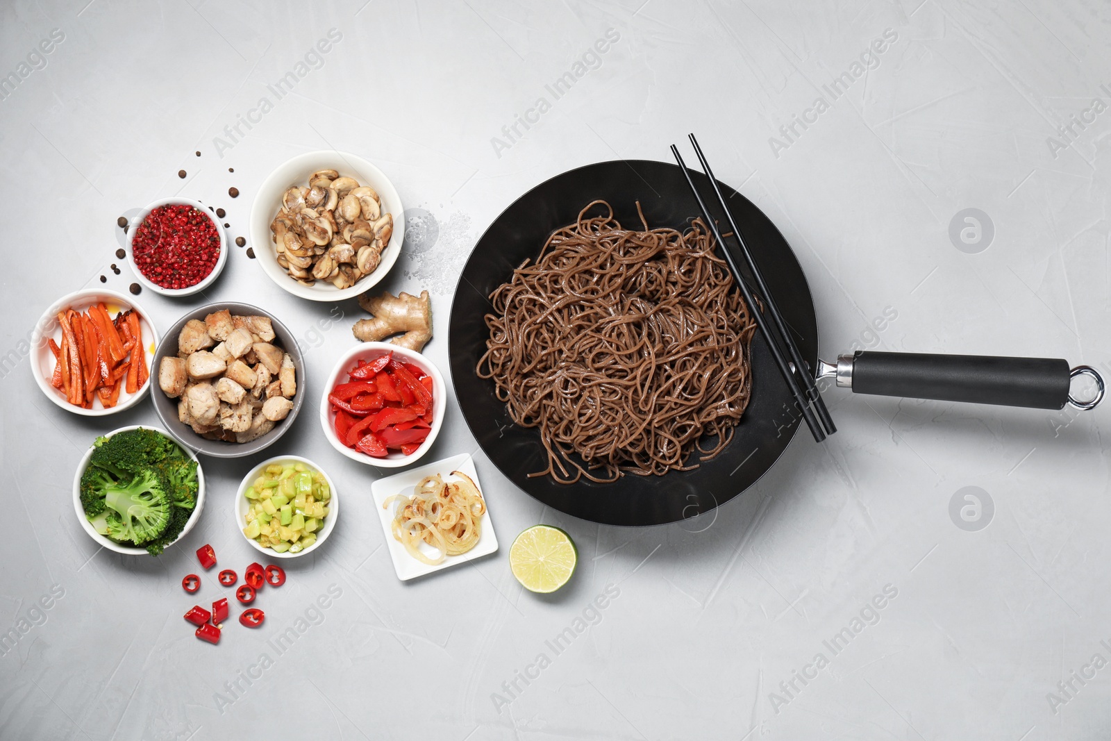 Photo of Wok with noodles, chicken and other products on light grey table, flat lay