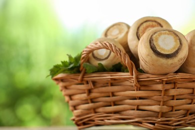 Photo of Wicker basket with delicious fresh ripe parsnips on wooden table outdoors, closeup