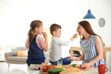 Photo of Young woman cooking breakfast for her children in kitchen. Happy family