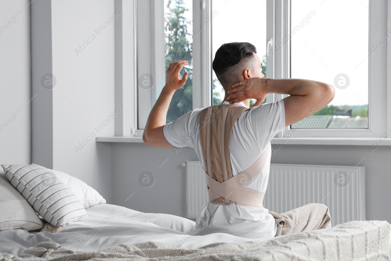 Photo of Man with orthopedic corset sitting in bedroom, back view