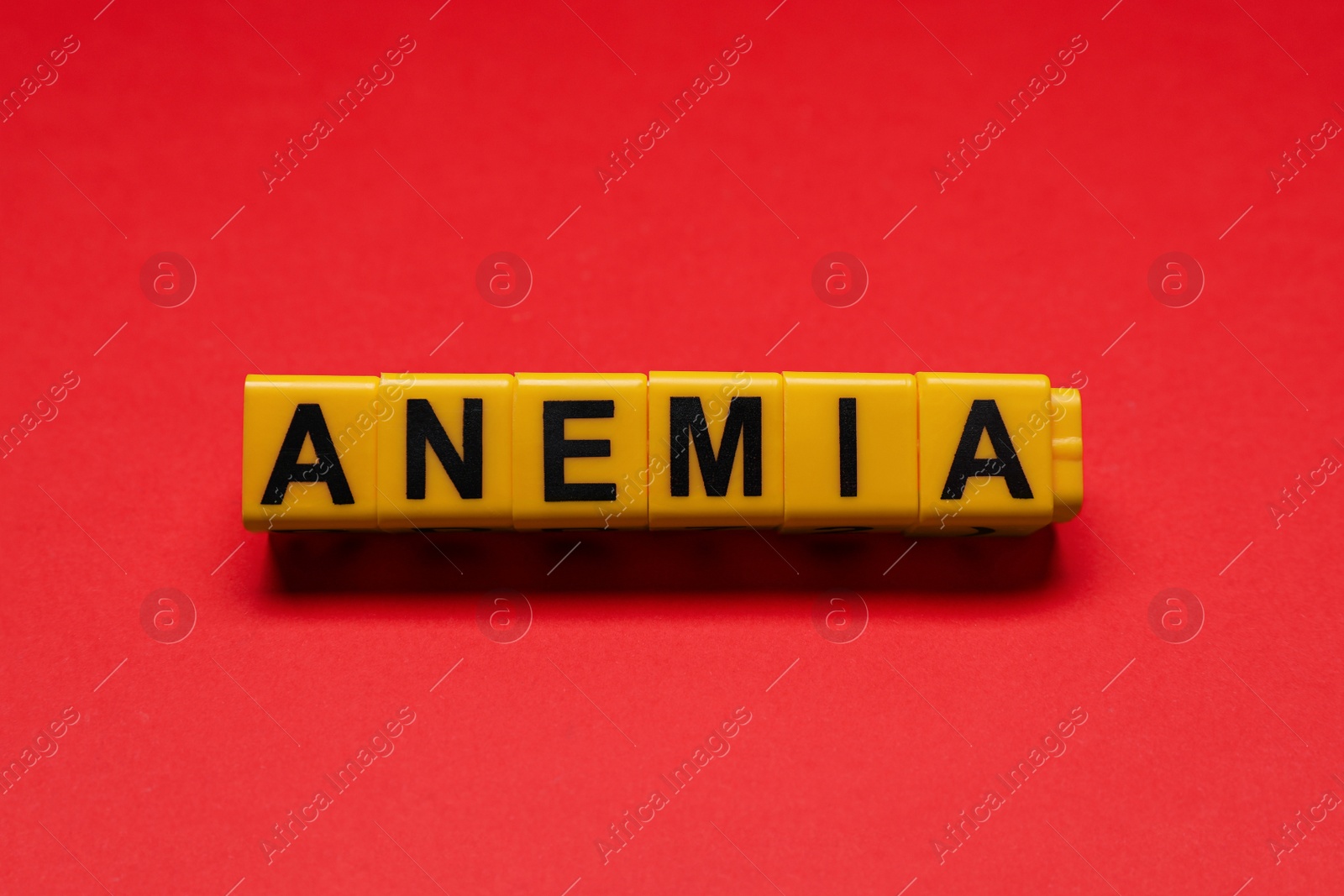Photo of Word Anemia made of yellow cubes on red background, flat lay