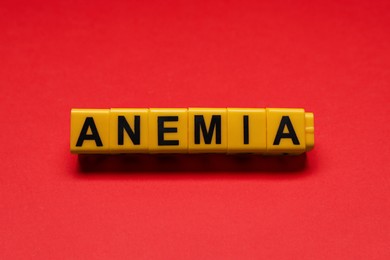Photo of Word Anemia made of yellow cubes on red background, flat lay