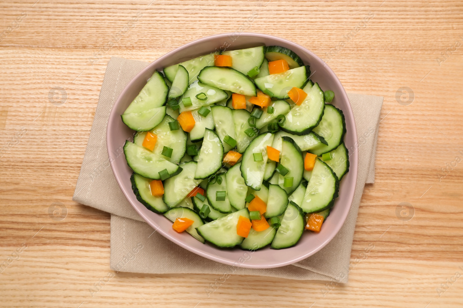 Photo of Tasty fresh salad with cucumber in bowl on wooden table, top view