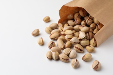 Overturned paper bag with pistachio nuts on white background, closeup. Space for text
