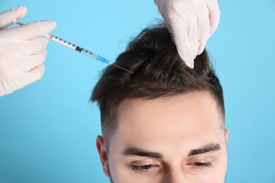 Photo of Young man with hair loss problem receiving injection on color background, closeup