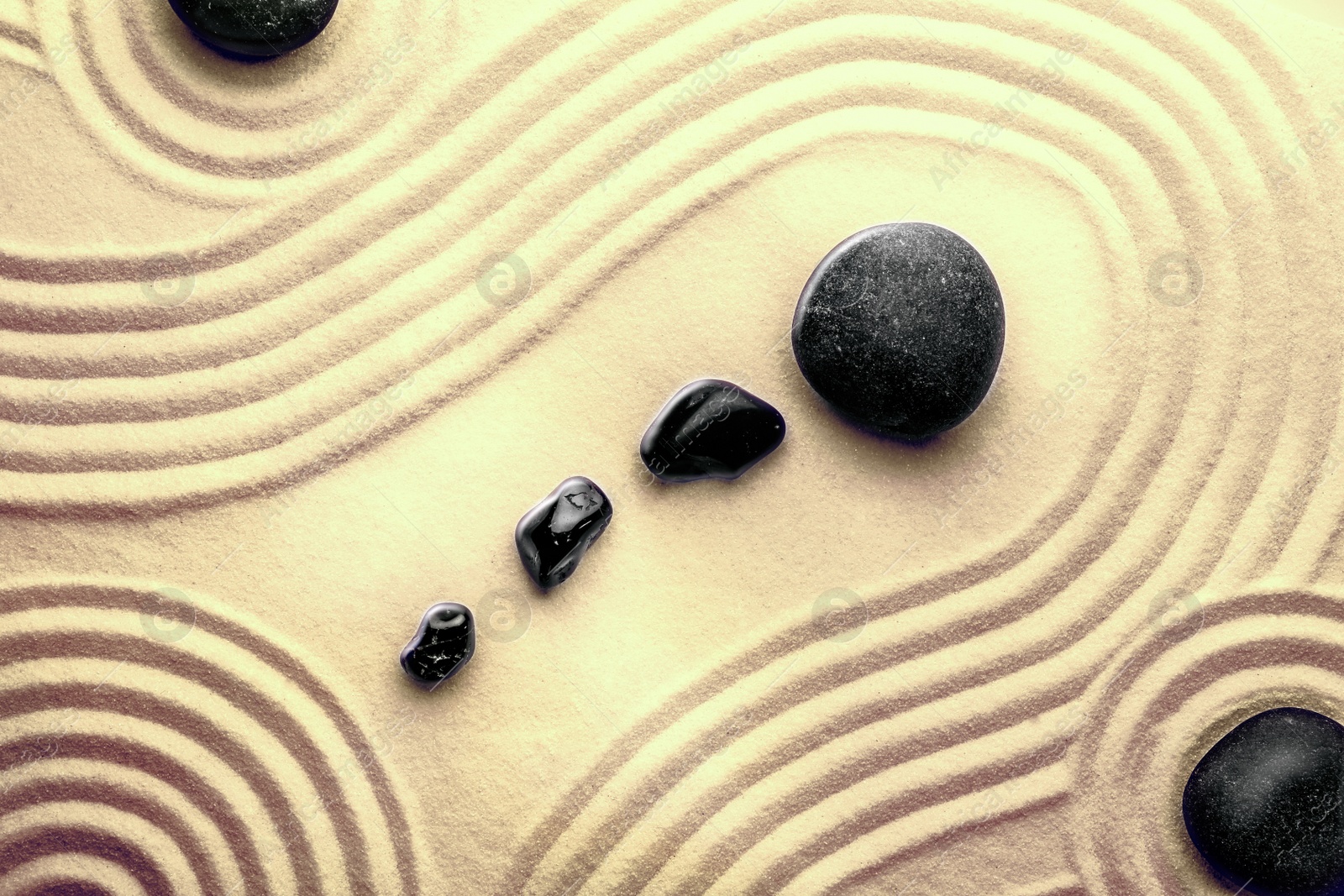 Image of Black stones on sand with pattern, top view. Zen, meditation, harmony