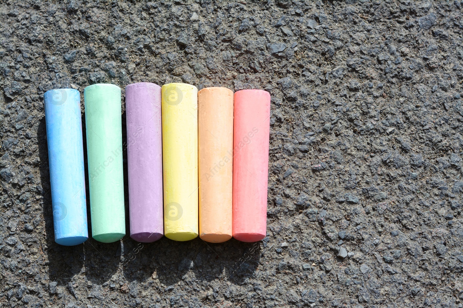 Photo of Colorful chalk sticks on asphalt, flat lay. Space for text