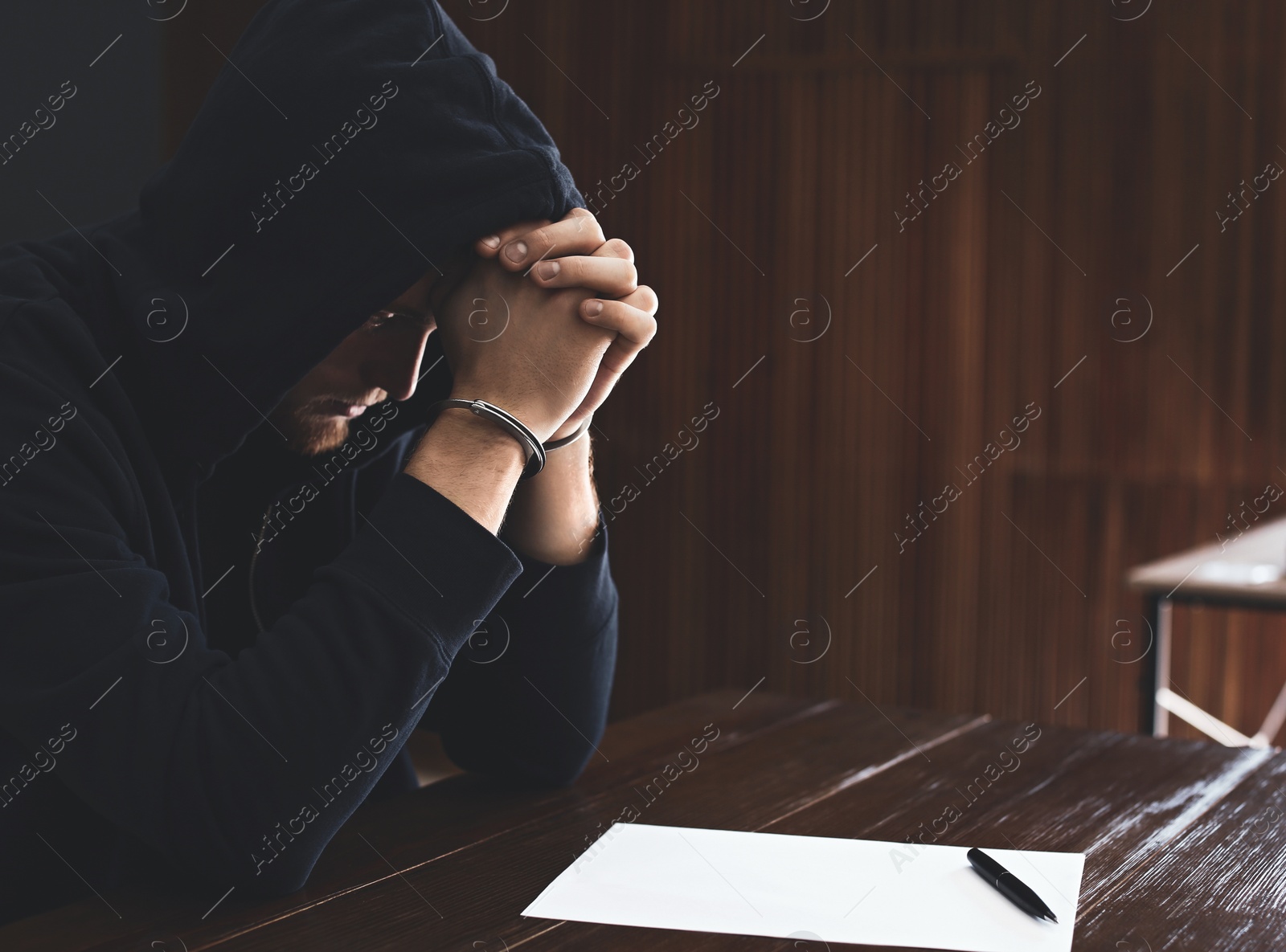 Photo of Criminal in handcuffs with confession at desk indoors. Space for text