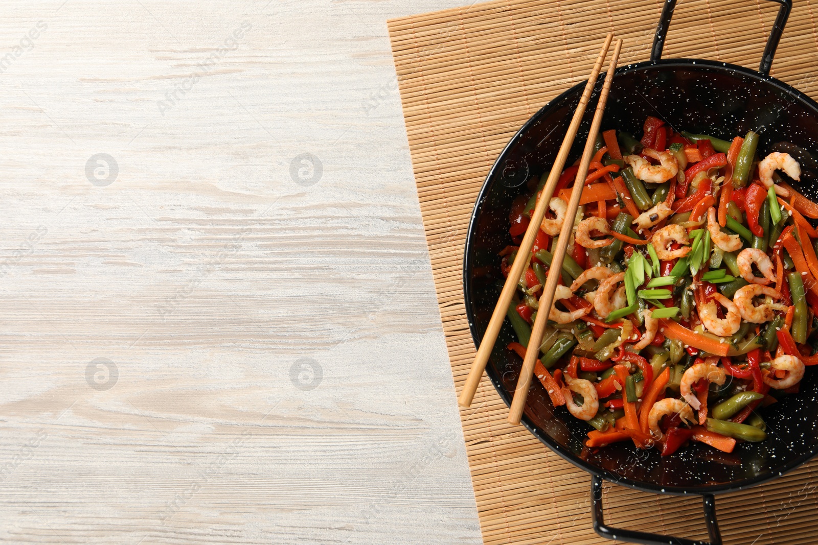 Photo of Shrimp stir fry with vegetables in wok and chopsticks on wooden table, top view. Space for text