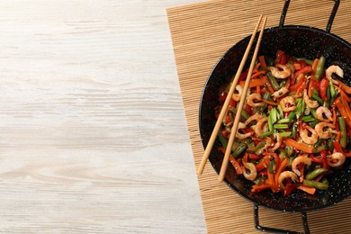 Shrimp stir fry with vegetables in wok and chopsticks on wooden table, top view. Space for text