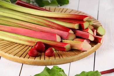 Photo of Cut fresh rhubarb stalks and strawberries on white wooden table, closeup