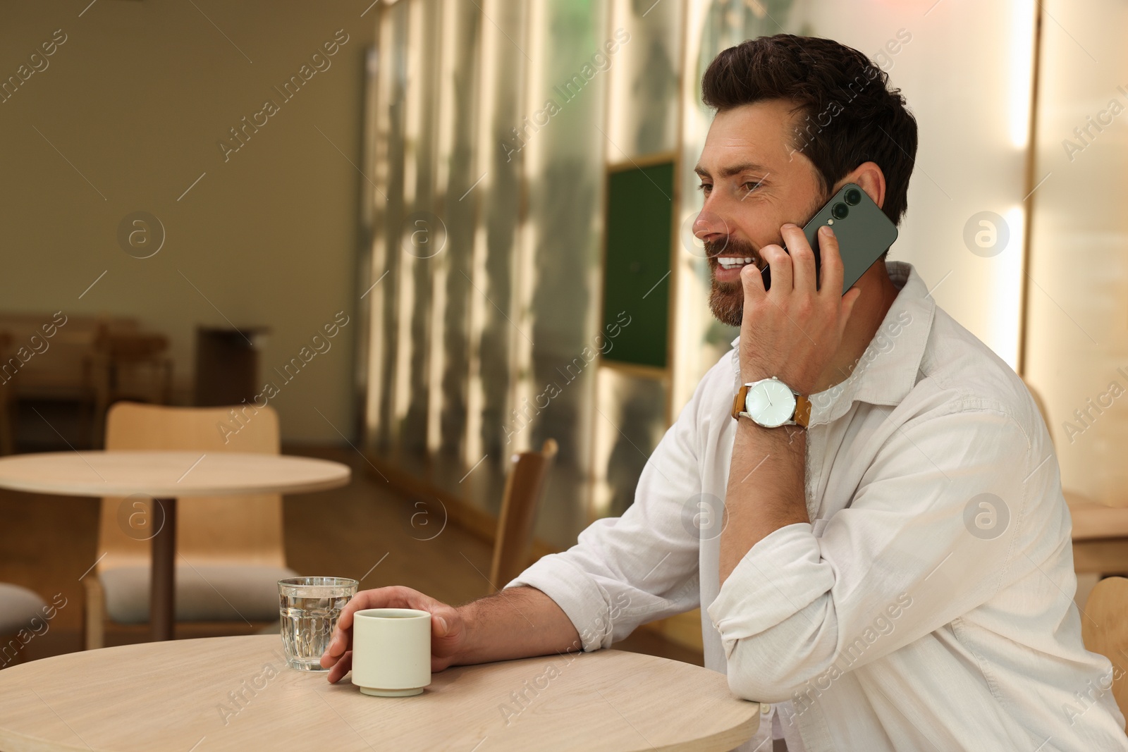 Photo of Handsome man talking on phone at table in cafe