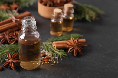 Bottle of essential oil, anise, cinnamon and fir tree branches on black table