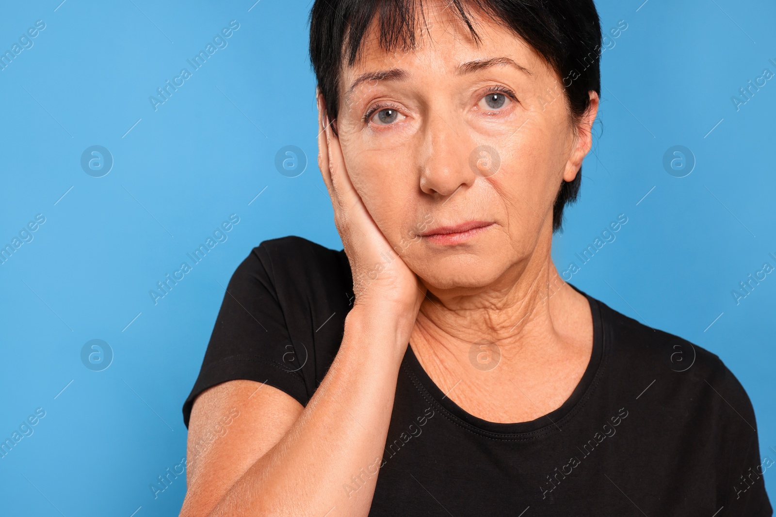 Photo of Senior woman suffering from ear pain on light blue background, closeup