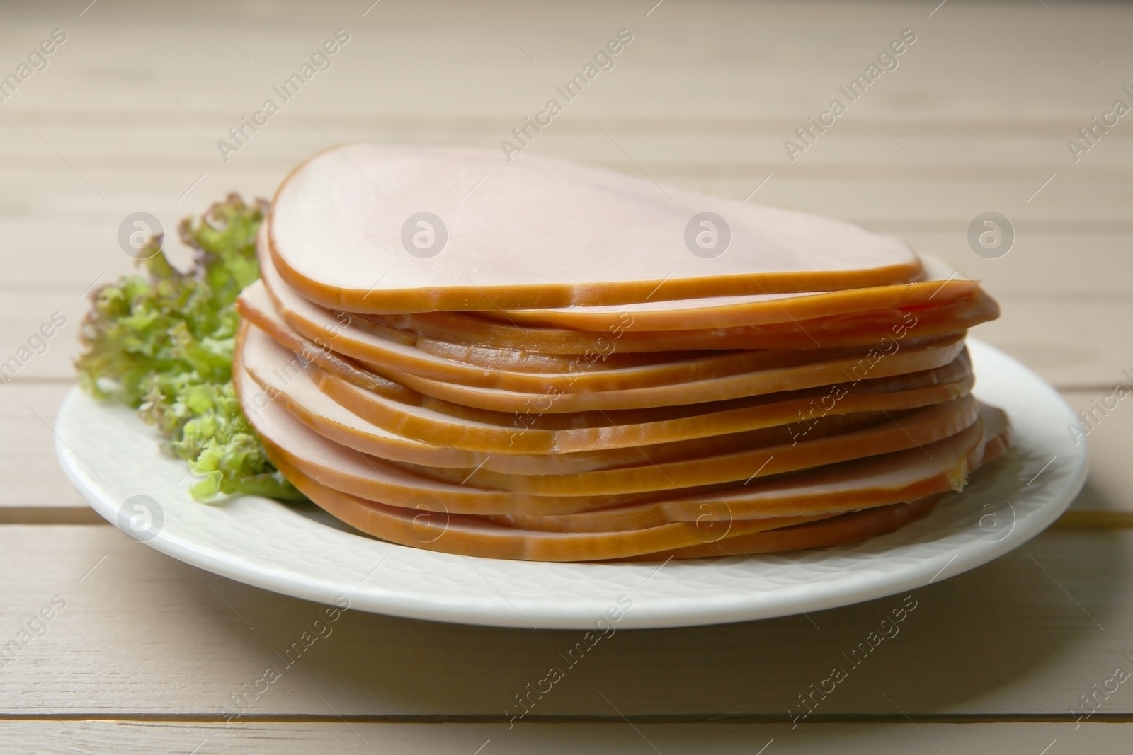 Photo of Slices of delicious boiled sausage with lettuce on beige wooden table, closeup