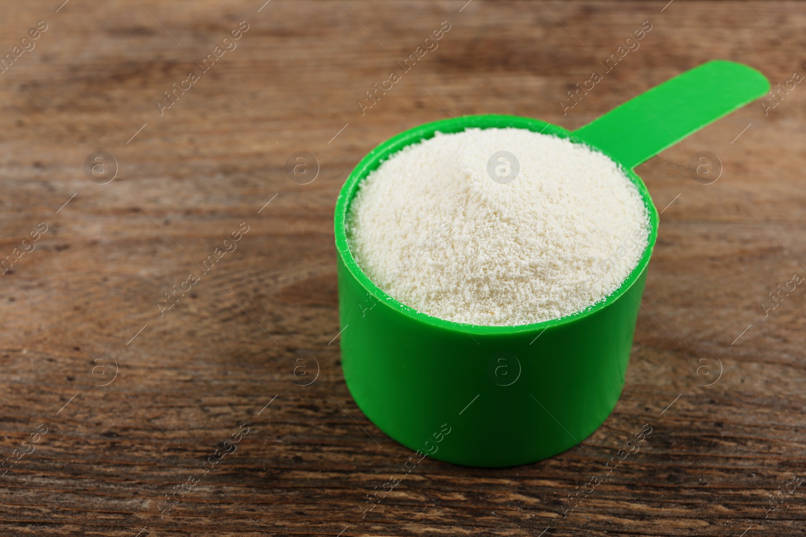 Photo of Measuring scoop of protein powder on wooden table, closeup. Space for text