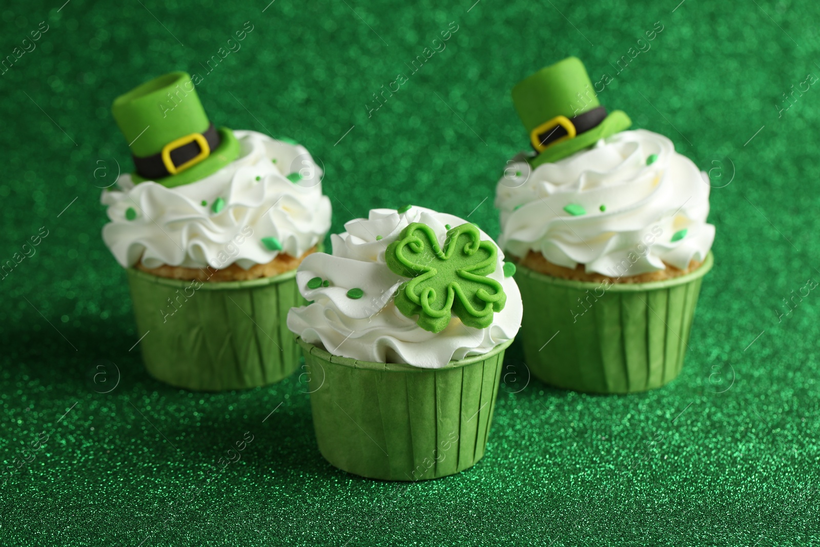 Photo of St. Patrick's day party. Tasty festively decorated cupcakes on shiny green surface, closeup