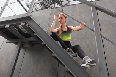 Beautiful woman in stylish gym clothes sitting on stairs on street, low angle view