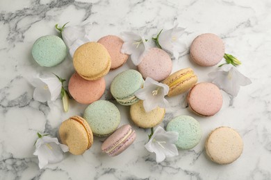 Photo of Delicious macarons and flowers on white marble table, flat lay